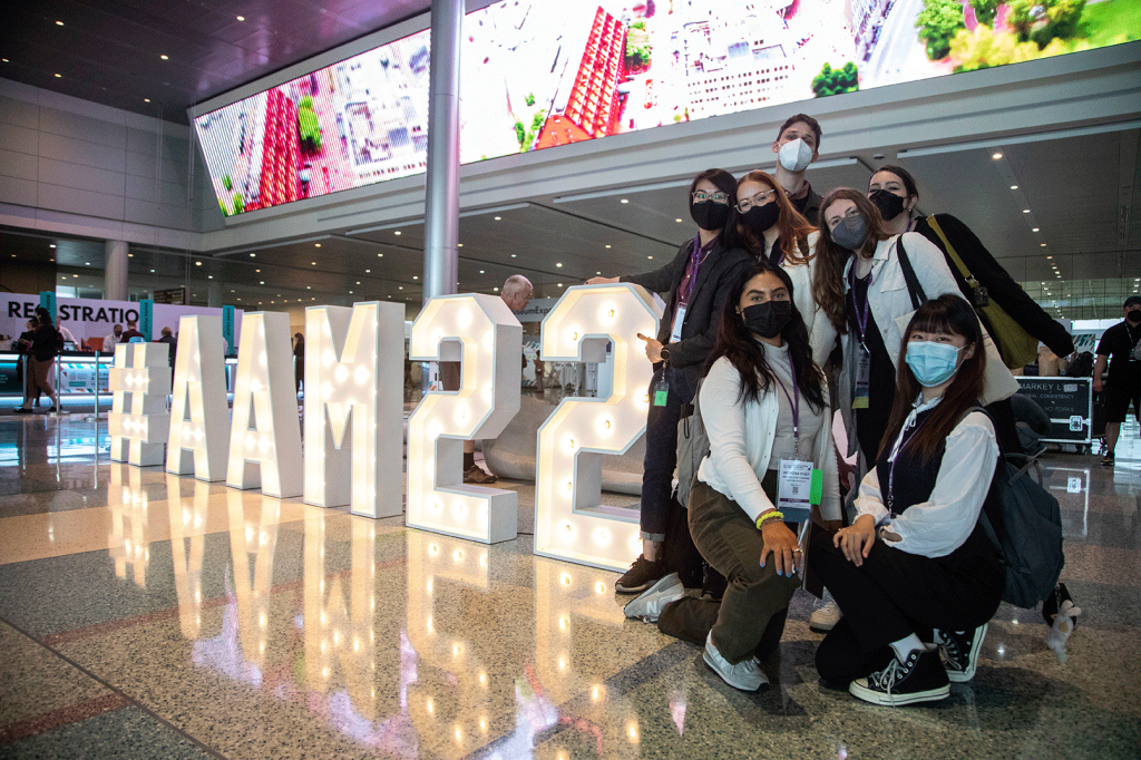 Photo of attendees posing in front of an #AAM22 neon sign